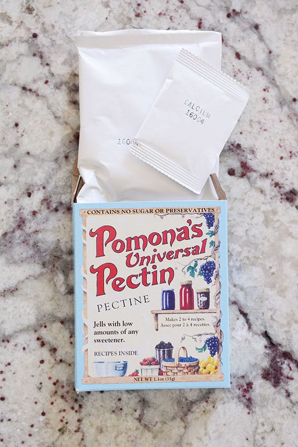 A box of Pomona's Universal Pectin with the packets coming out on a kitchen countertop.