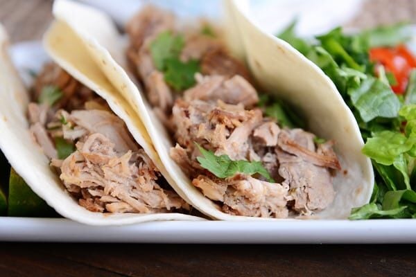 Side view of two shredded pork tacos next to a green salad.