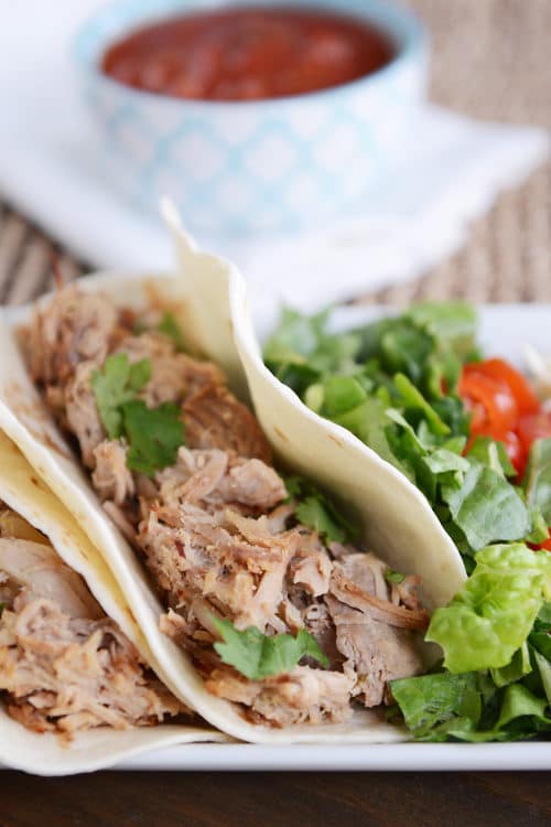 A shredded pork taco in a flour tortilla next to lettuce and tomatoes. 