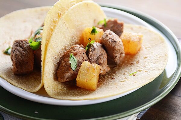 Two pork and pineapple tacos in corn tortillas. 