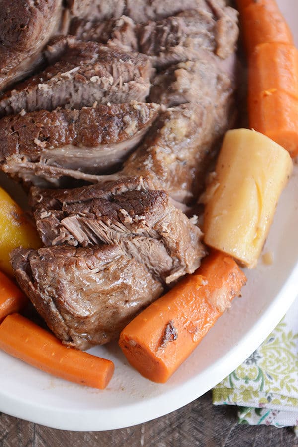 Top view of a pot roast sliced up with cooked carrots and potatoes around it.