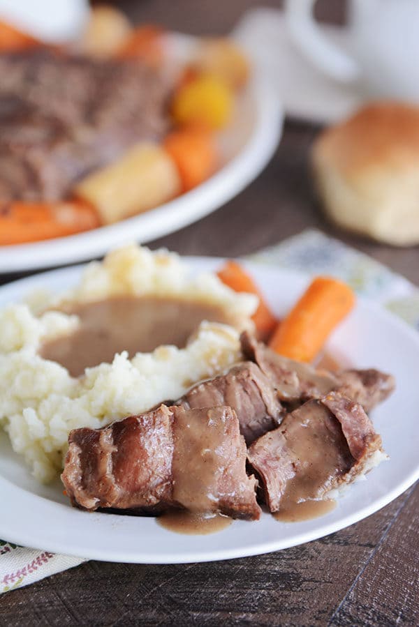 A plate of pot roast with gravy, mashed potatoes, and carrots. 