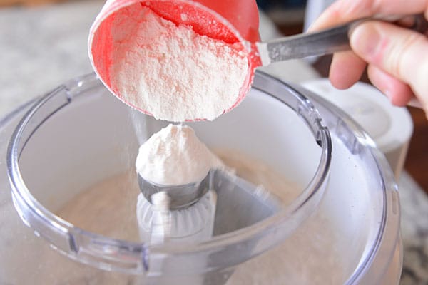 White flour getting dumped into a Bosch mixer bowl.