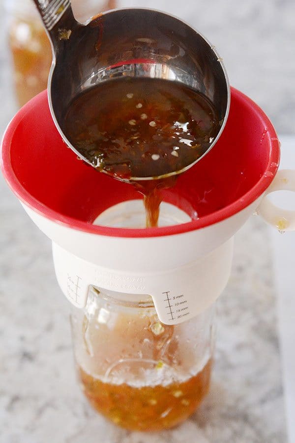 A ladle of jalapeno jelly getting funneled into a glass mason jar.