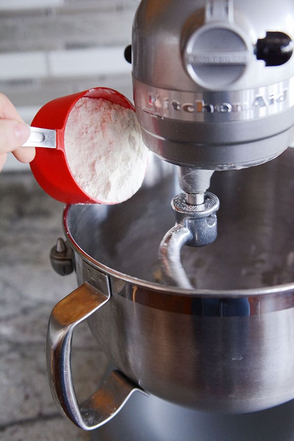 White flour getting poured into a KitchenAid bowl.