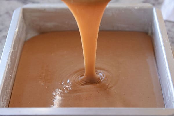 Liquid caramel getting poured into a metal tin. 