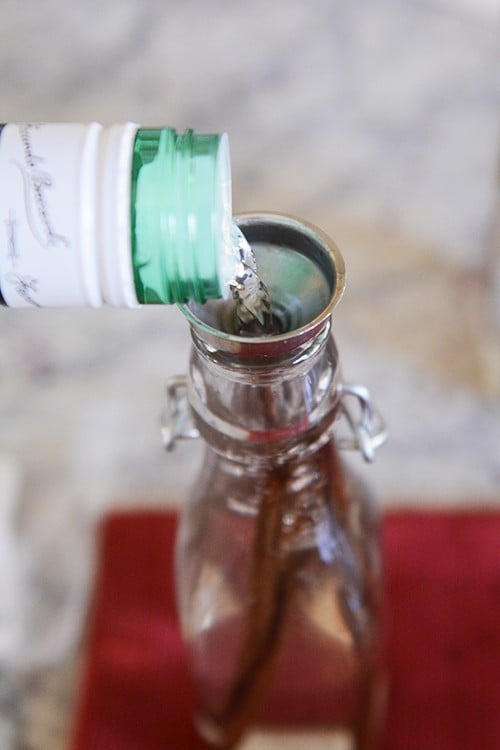 Alcohol getting poured into a glass bottle with vanilla beans.