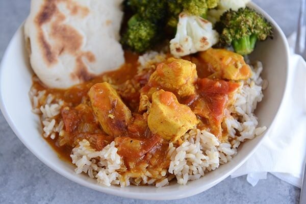 Top view of a bowl full or rice topped with chicken curry, veggies, and flatbread.