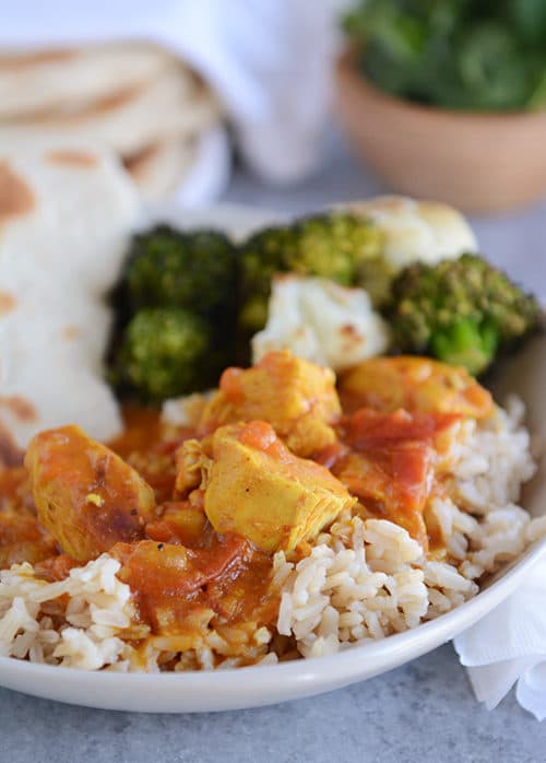 A white bowl of rice topped with chicken curry and vegetables.