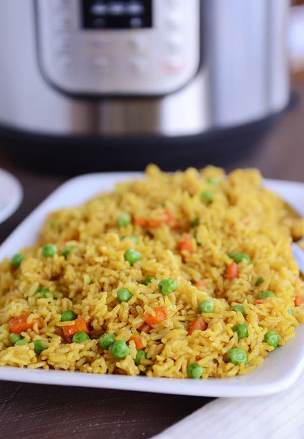 A white plate full of rice with peas and carrots sprinkled throughout, and an Instant Pot in the background.