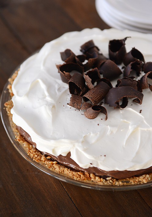 A pie with whipped topping and chocolate curls in a glass pie dish.