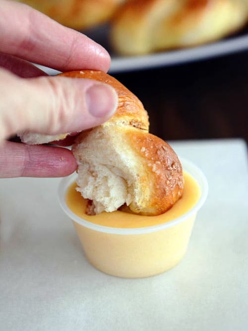 A chunk of pretzel twist being dunked in cheese sauce.