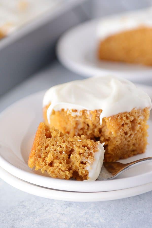 A fork taking a bite out of a frosted pumpkin bar on a white plate.