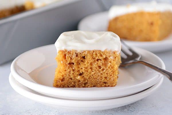 A frosted pumpkin bar on a white plate with a fork on the side.