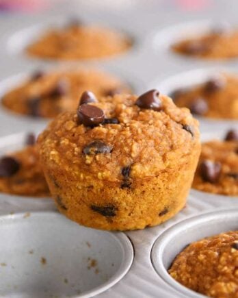 Easy pumpkin blender muffins in muffin tin with one muffin sitting on top.