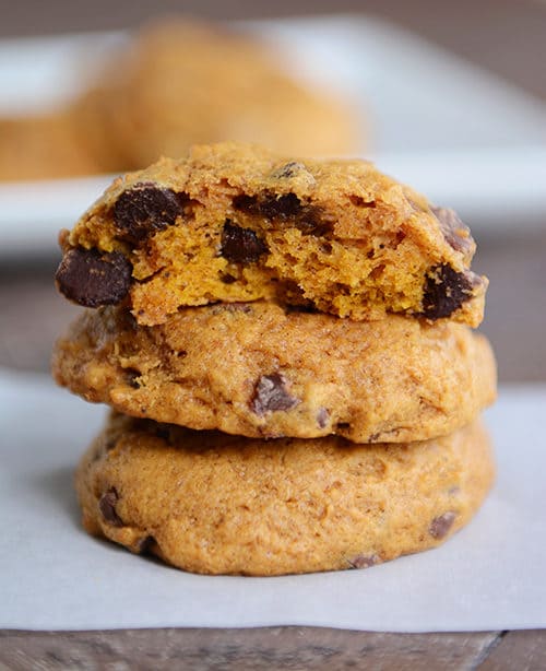 A stack of chocolate chip pumpkin cookies with the top cookie split in half on a piece of parchment paper.