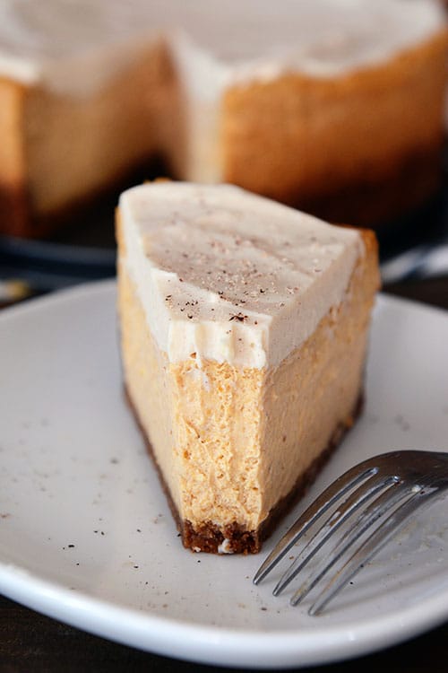 A thick slice of pumpkin cheesecake with a bite taken out on a white plate.