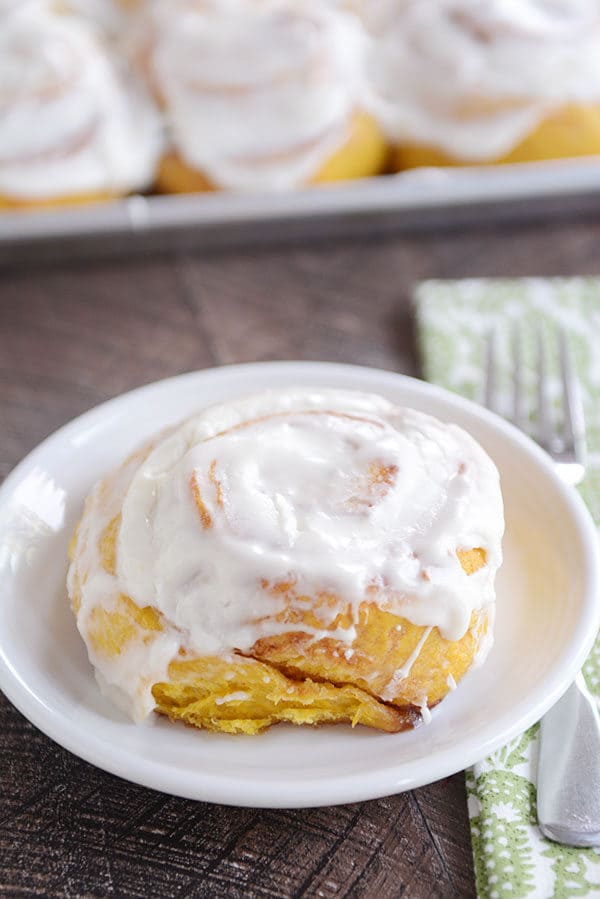 A frosted pumpkin cinnamon roll on a white plate.