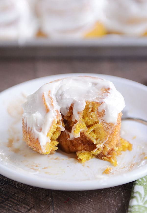 The center of a frosted pumpkin cinnamon roll with a bite taken out on a white plate.