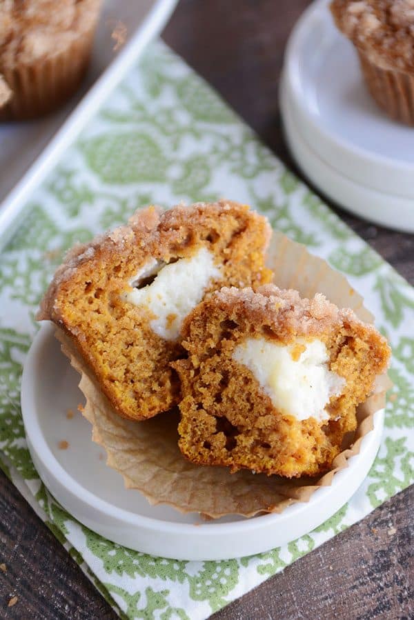 A cream cheese filled pumpkin muffin split in half on a white ramekin.