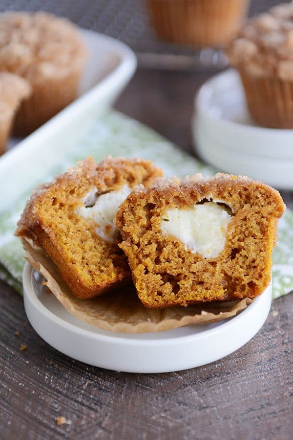 A cream cheese filled pumpkin muffin split in half on a white ramekin.