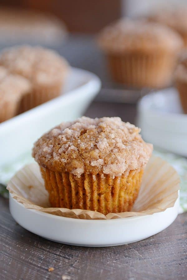 A pumpkin muffin sitting on its liner and a white ramekin. 