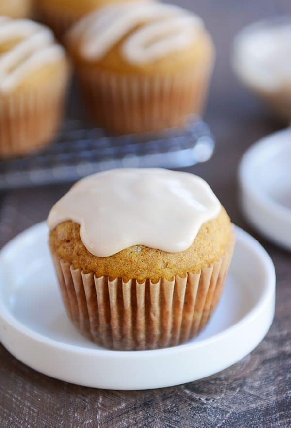A pumpkin muffin covered in maple frosting sitting on a white ramekin.