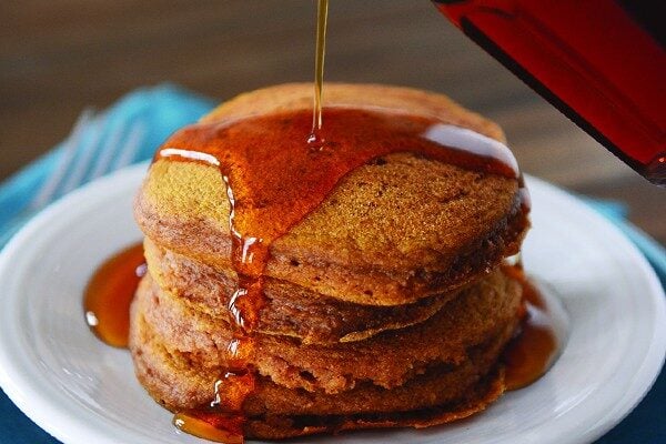 A stack of pumpkin pancakes getting syrup poured over them. 