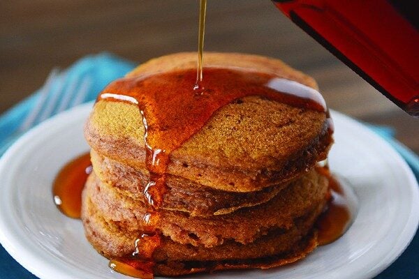 A stack of pumpkin pancakes getting syrup poured over them.