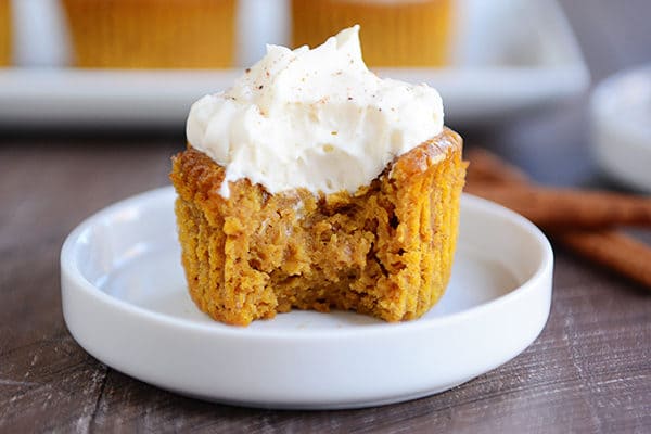 A pumpkin pie cupcake on a white plate with a bite taken out and whipped topping on top.