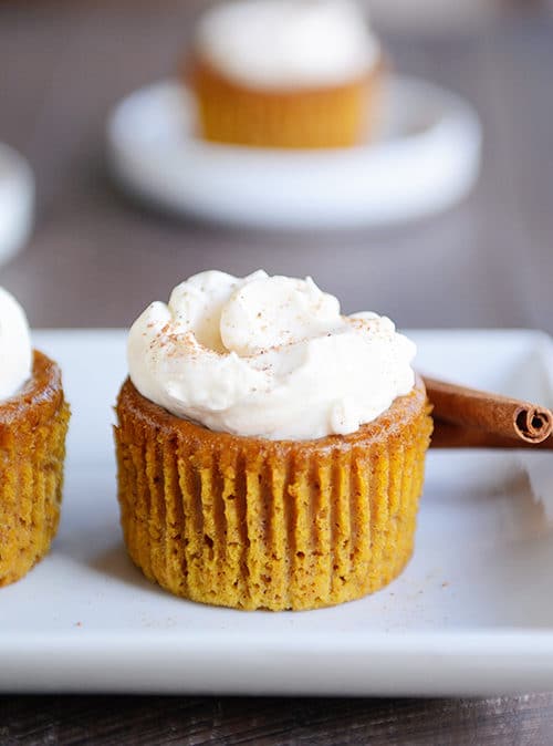 A crustless pumpkin pie cupcake with whipped topping and cinnamon sticks next to it.