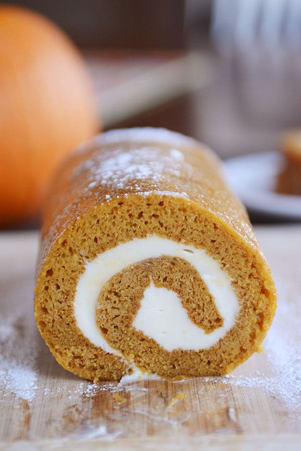 A front view of a pumpkin roll with a cream cheese swirl in it on a cutting board. 