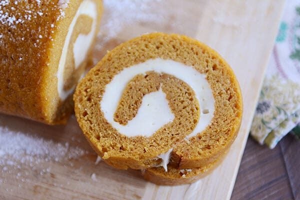 Two slices of a cream cheese swirl pumpkin roll cut off of the rest of the roll on a wooden cutting board.