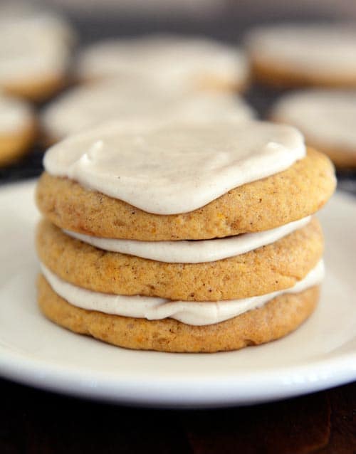 A stack of frosted pumpkin sugar cookies on a white plate. 