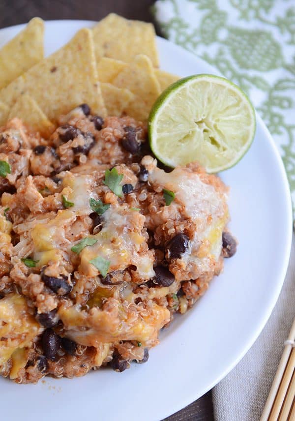 A white plate of tortillas chips, a helping of a cheesy black bean quinoa bake, and a half lime.