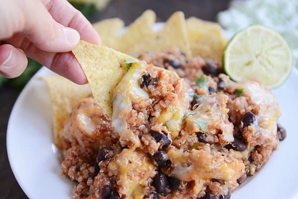 A tortilla chip dipping into a black bean cheesy quinoa mixture. 