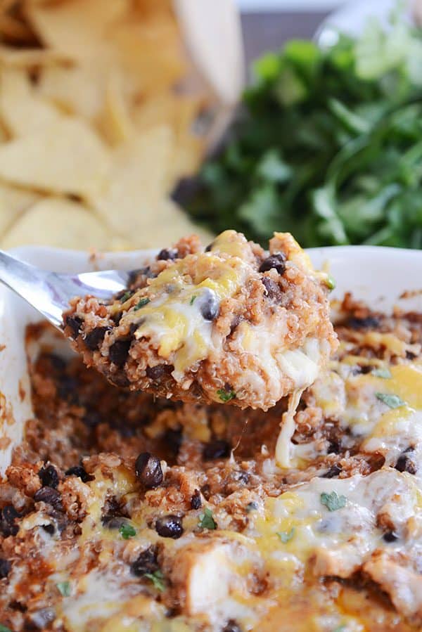 A large metal spoon taking a scoop of black bean cheesy quinoa bake out of a white casserole dish.