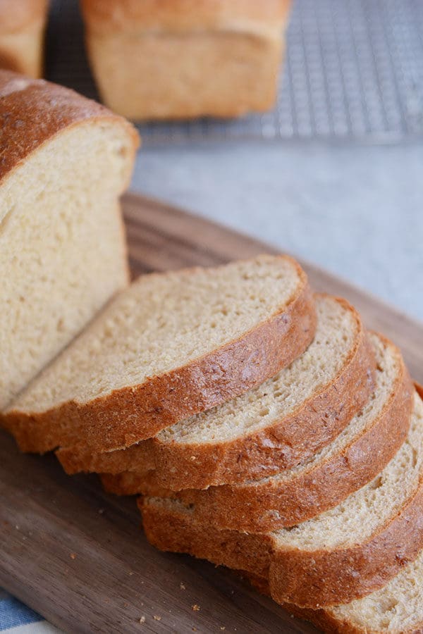 A loaf of wheat bread with thick slices cut off of it on a wooden cutting board.