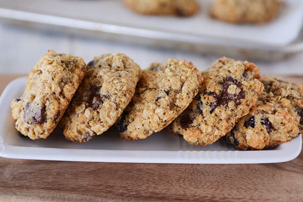 Five chocolate chip cookies leaning on each other on a white butter dish. 