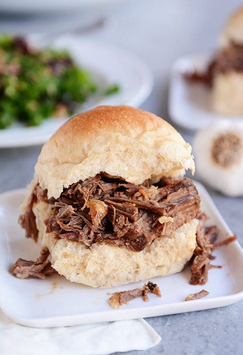 A roll cut in half and filled with shredded beef on a white plate. 