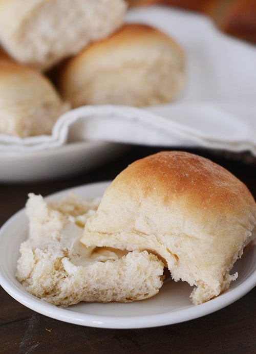 A roll split open on a white plate with more rolls in the background.