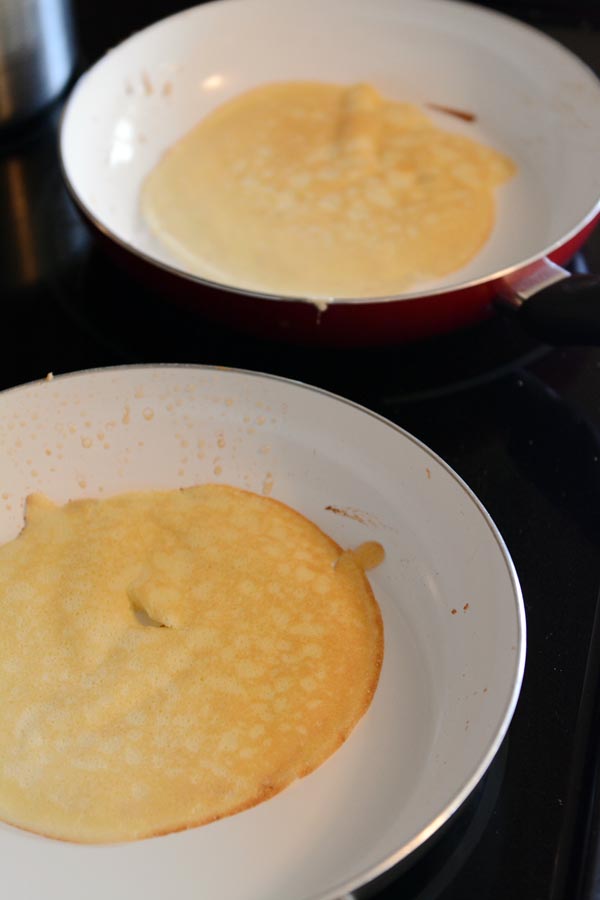 Two skillets with a flat cooked pancake in each one. 
