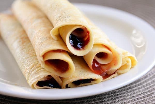 A white plate with six jam-filled rollup pancakes stacked on each other. 