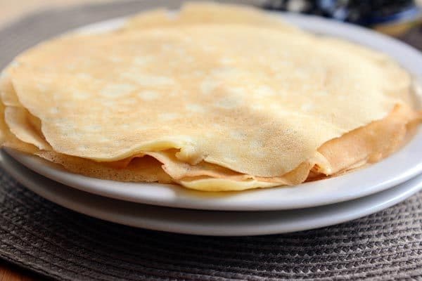 Two white plates with a stack of cooked crepes. 