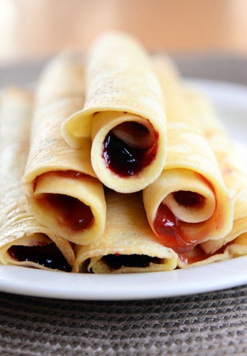 A side view of a white plate full of jam-filled rollup pancakes.