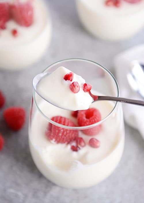 A spoon taking a bite of cream and berries out of a glass cup. 