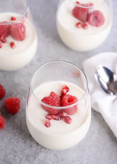 Glasses of cream topped with pomegranate seeds and raspberries.