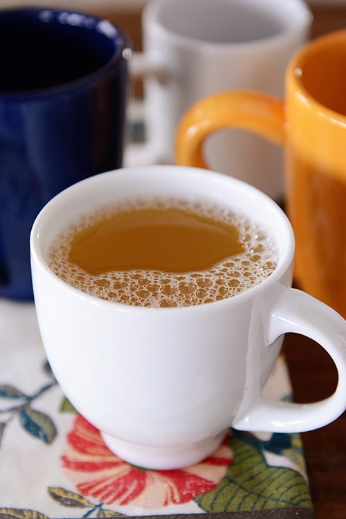 A white mug of tea with other empty mugs behind it. 