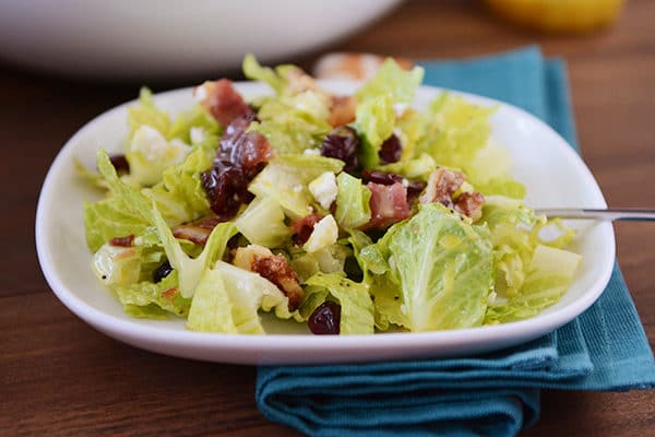 A white plate with romaine salad topped with craisins, feta, and bacon. 