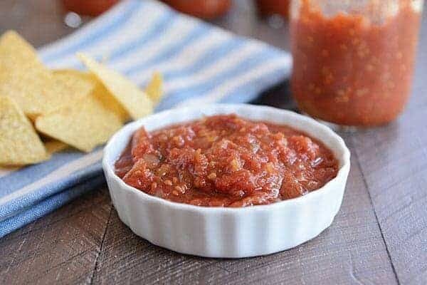 Ramekin of homemade salsa, in front of a half empty jar of salsa and tortilla chips.